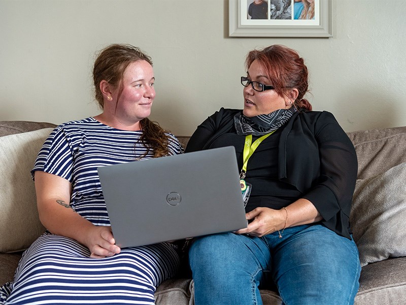 Two women looking at a laptop together on a sofa