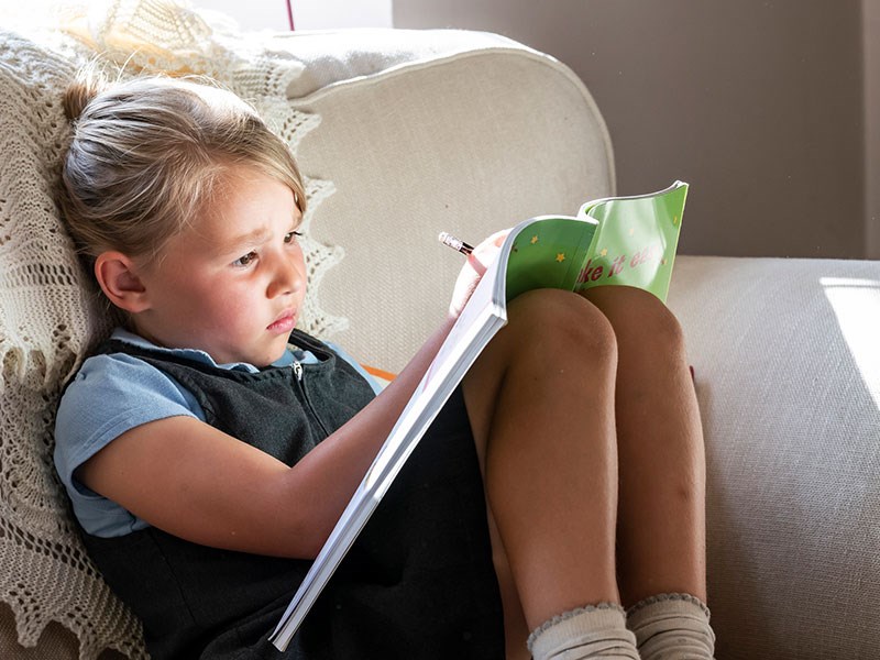 Image of small girl on sofa writing in book